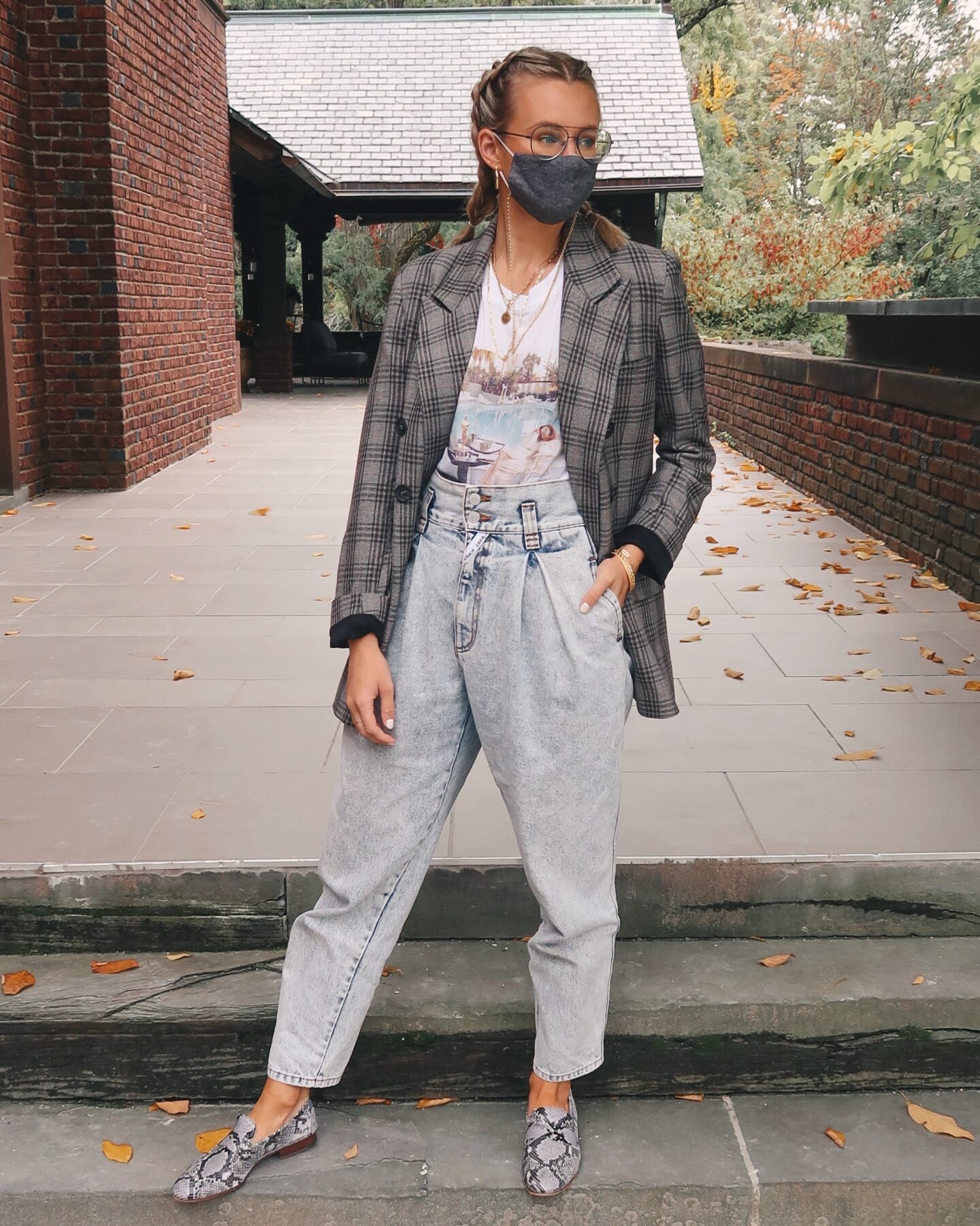 Girl with French braids, glasses and a mask wearing an oversized blazer, a tee shirt tucked into vintage jeans  and posing to showcase how to style loafers.