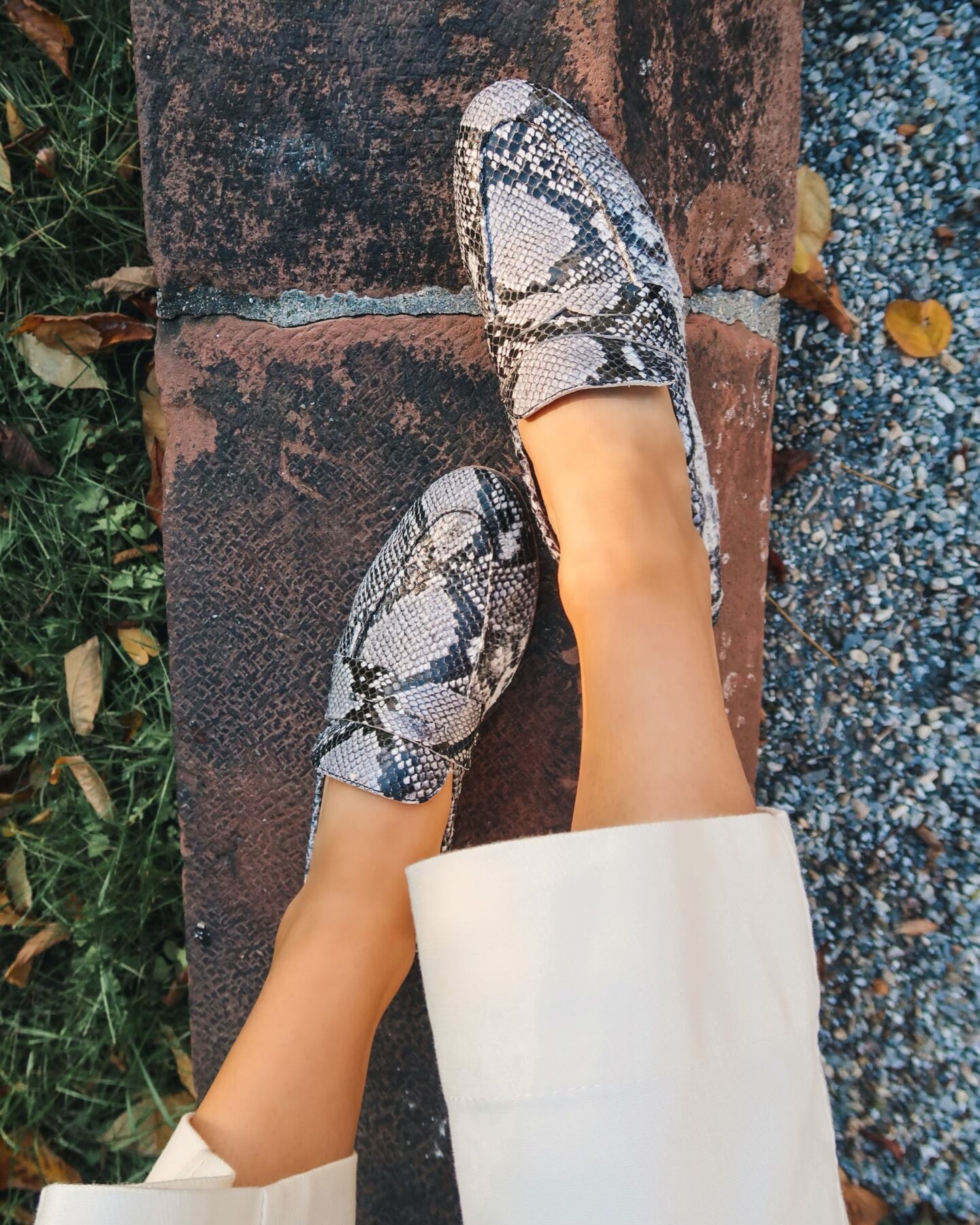 Close up photo of a woman wearing black and white snakeskin printed leather loafers.