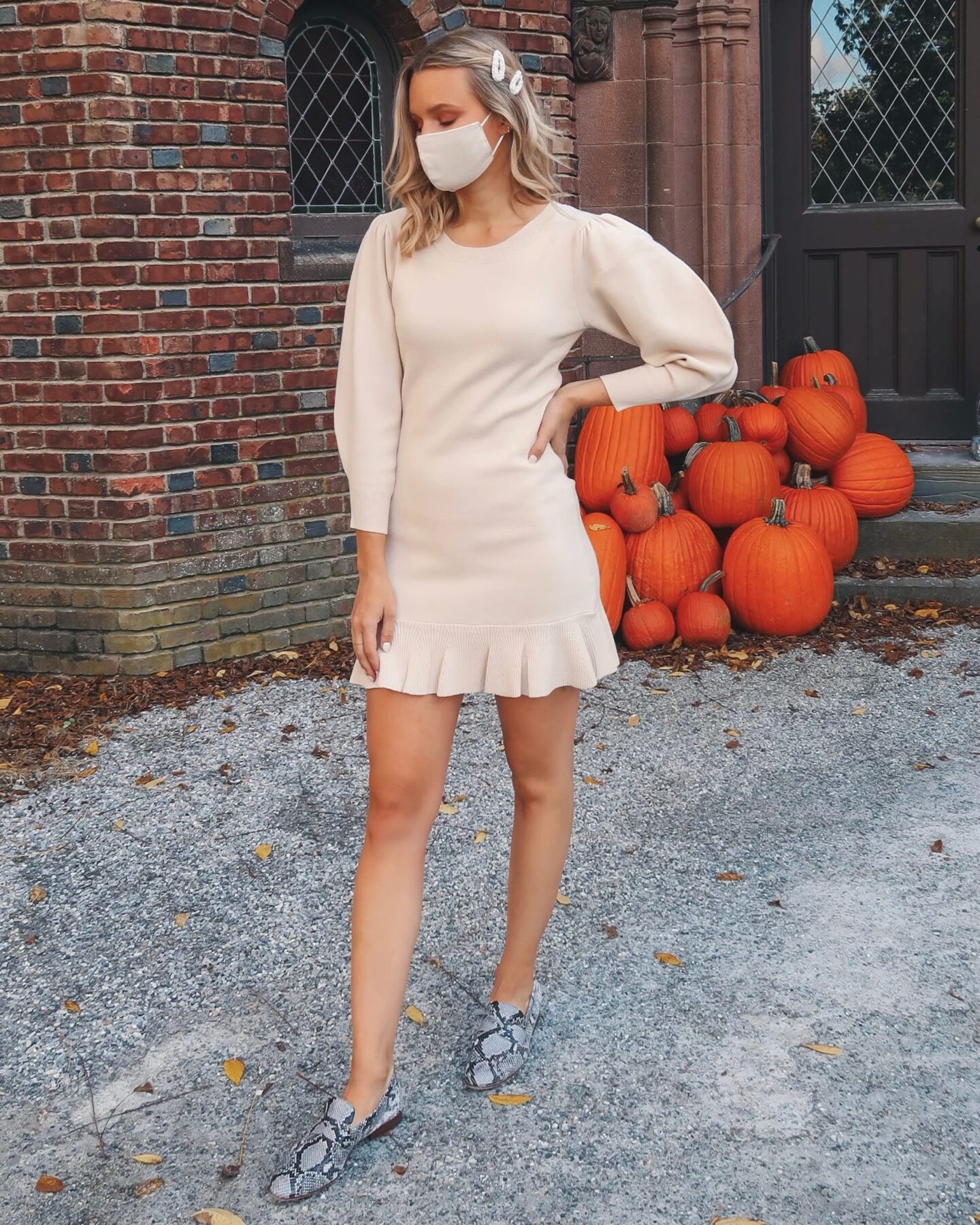 Blonde girl wearing a ruffled sweater mini dress, standing in front of a large group of pumpkins on the stairs to showcase how to style loafers