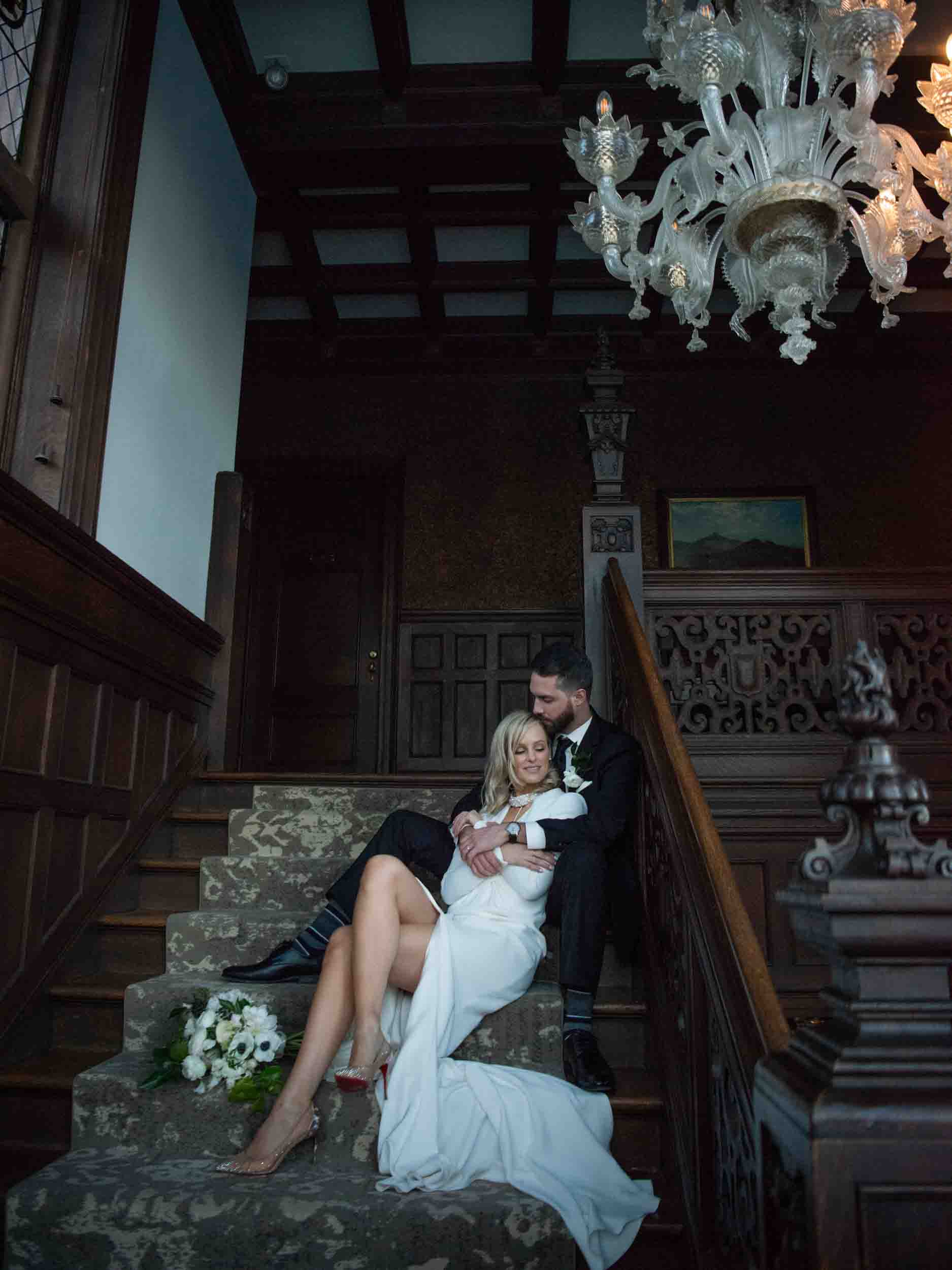Bride and groom cuddled up on the stairs of gilded-age manor