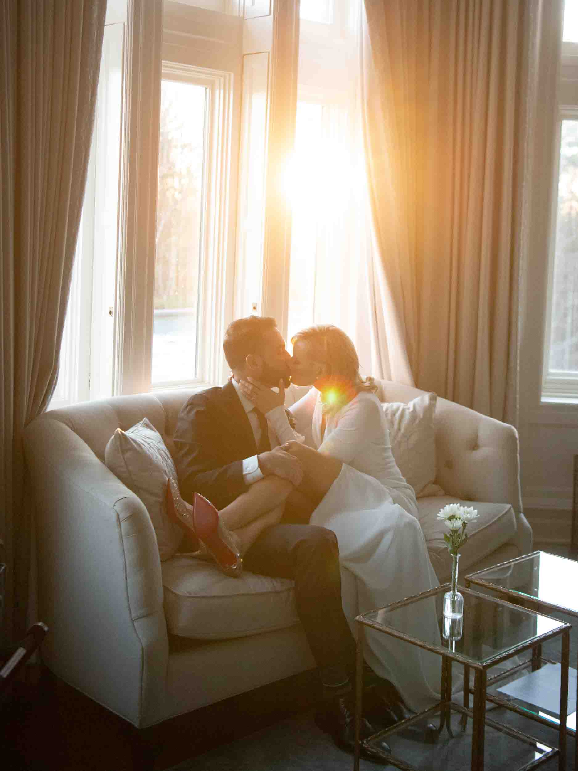Bride and groom kissing on the couch in the sunlight at golden hour