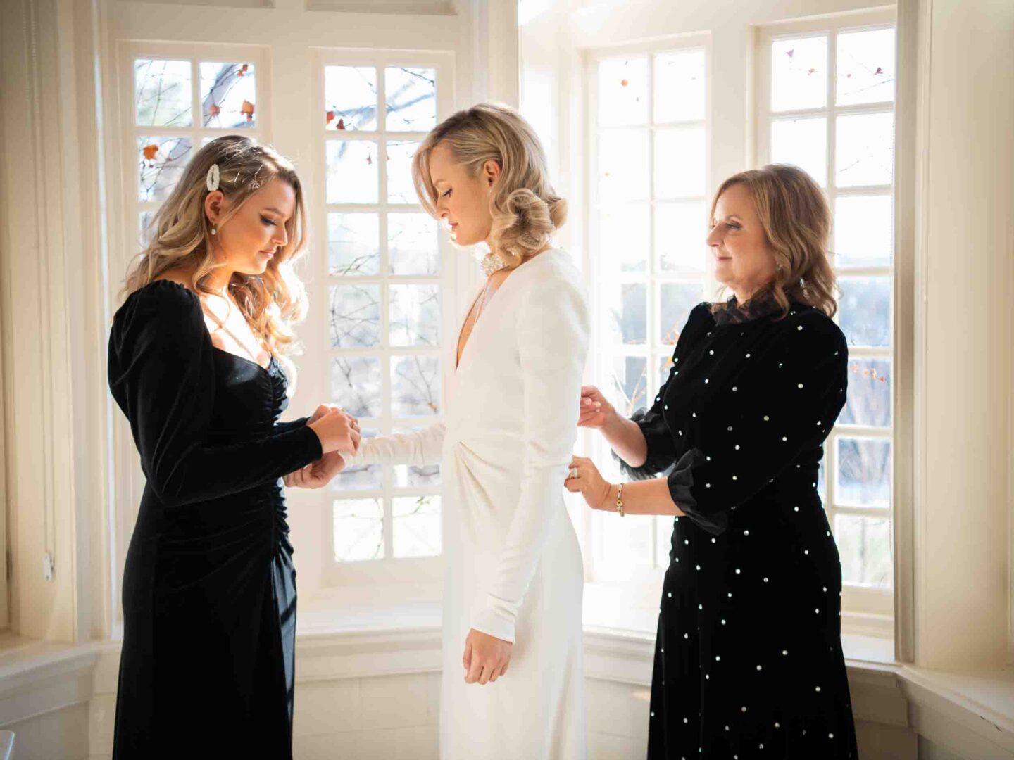 Mother and sister helping bride into her wedding dress